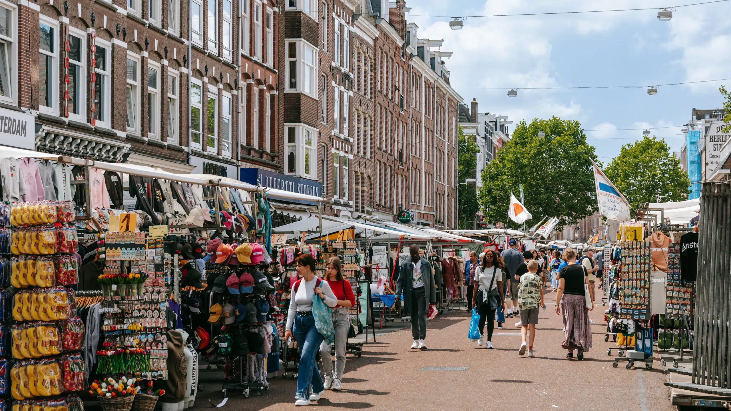 Shoppers walking past souvenir and clothing stalls at the Albert Cuyp Market in Amsterdam on a sunny day