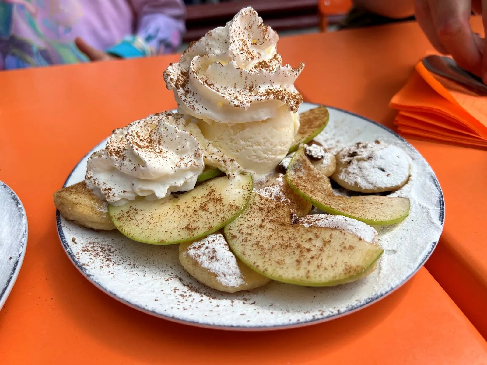 Dessert of sliced apple, ice cream and whipped cream dusted with cinnamon