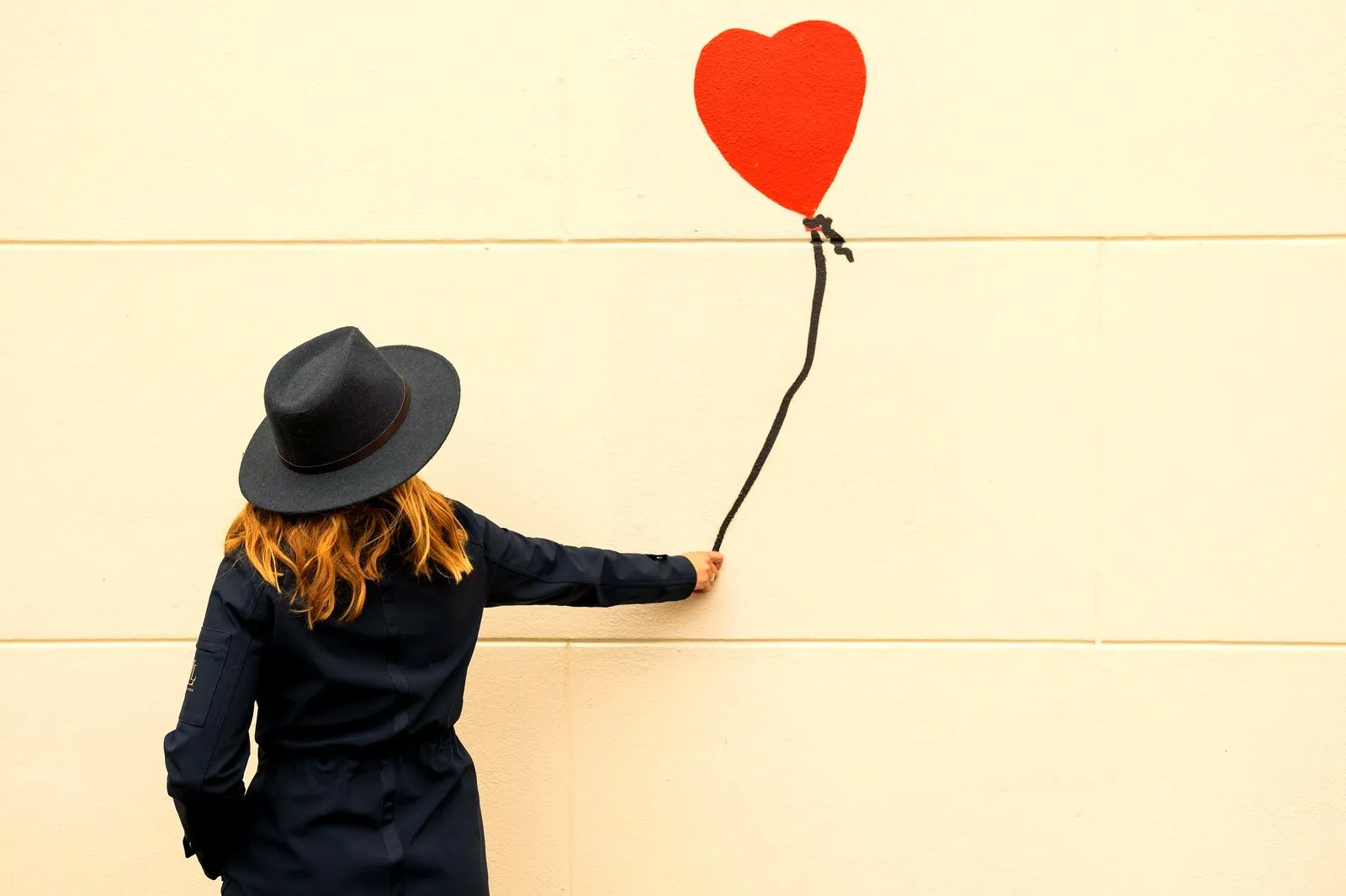 A guest reaching toward a Banksy-style red heart balloon painted on a wall in Amsterdam