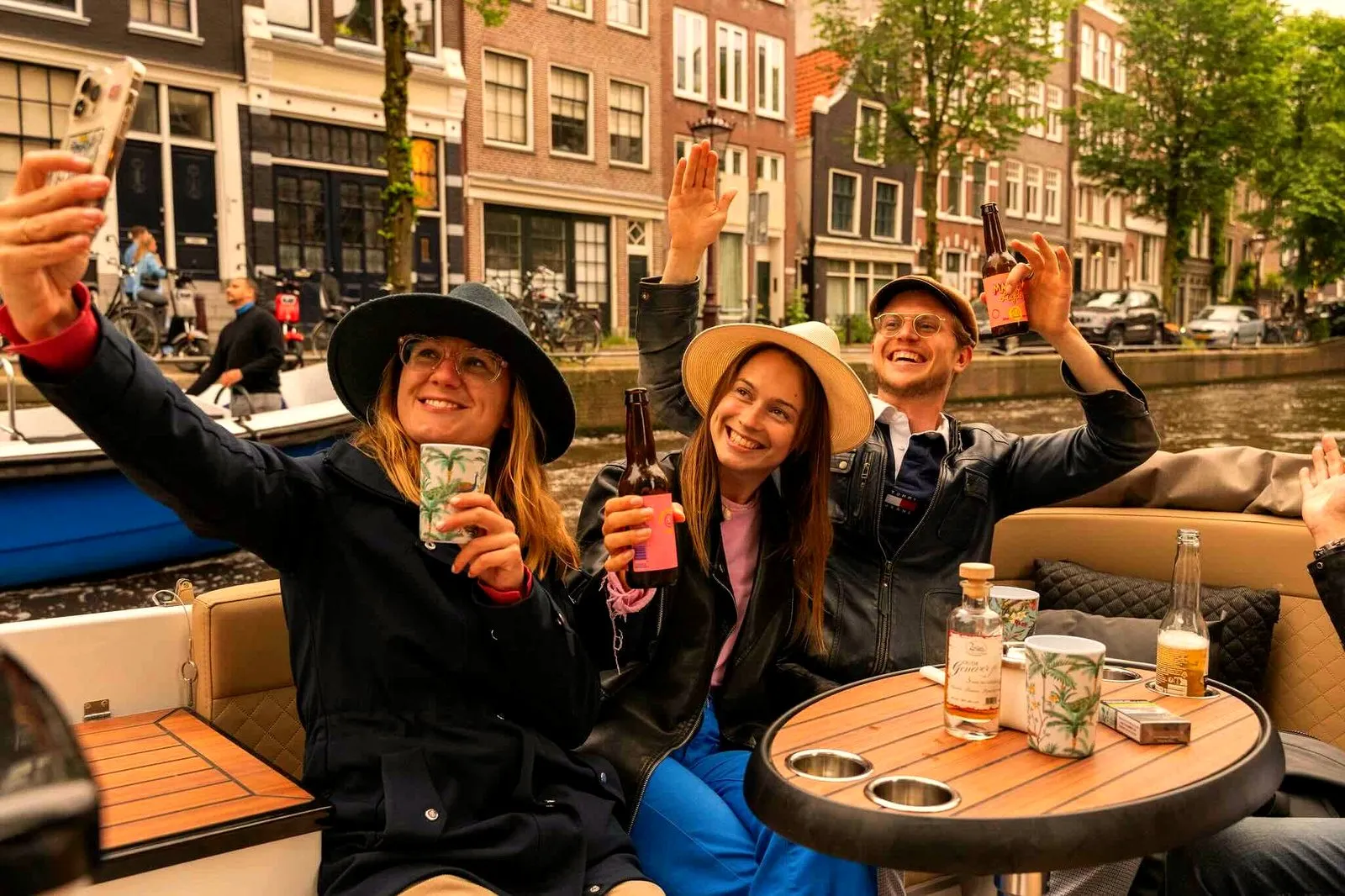 Three guests in hats taking a selfie with drinks on an Amsterdam canal boat
