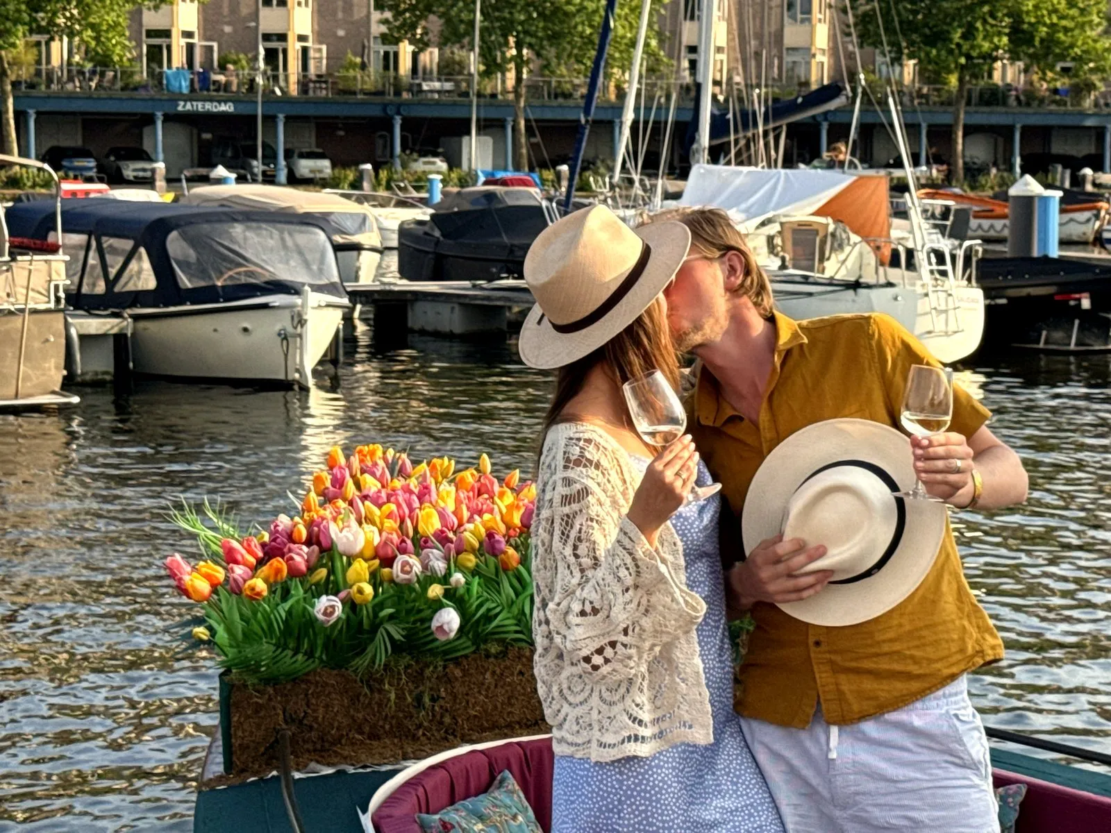 A couple kissing with raised wine glasses on an Amsterdam canal boat by the tulips at golden hour