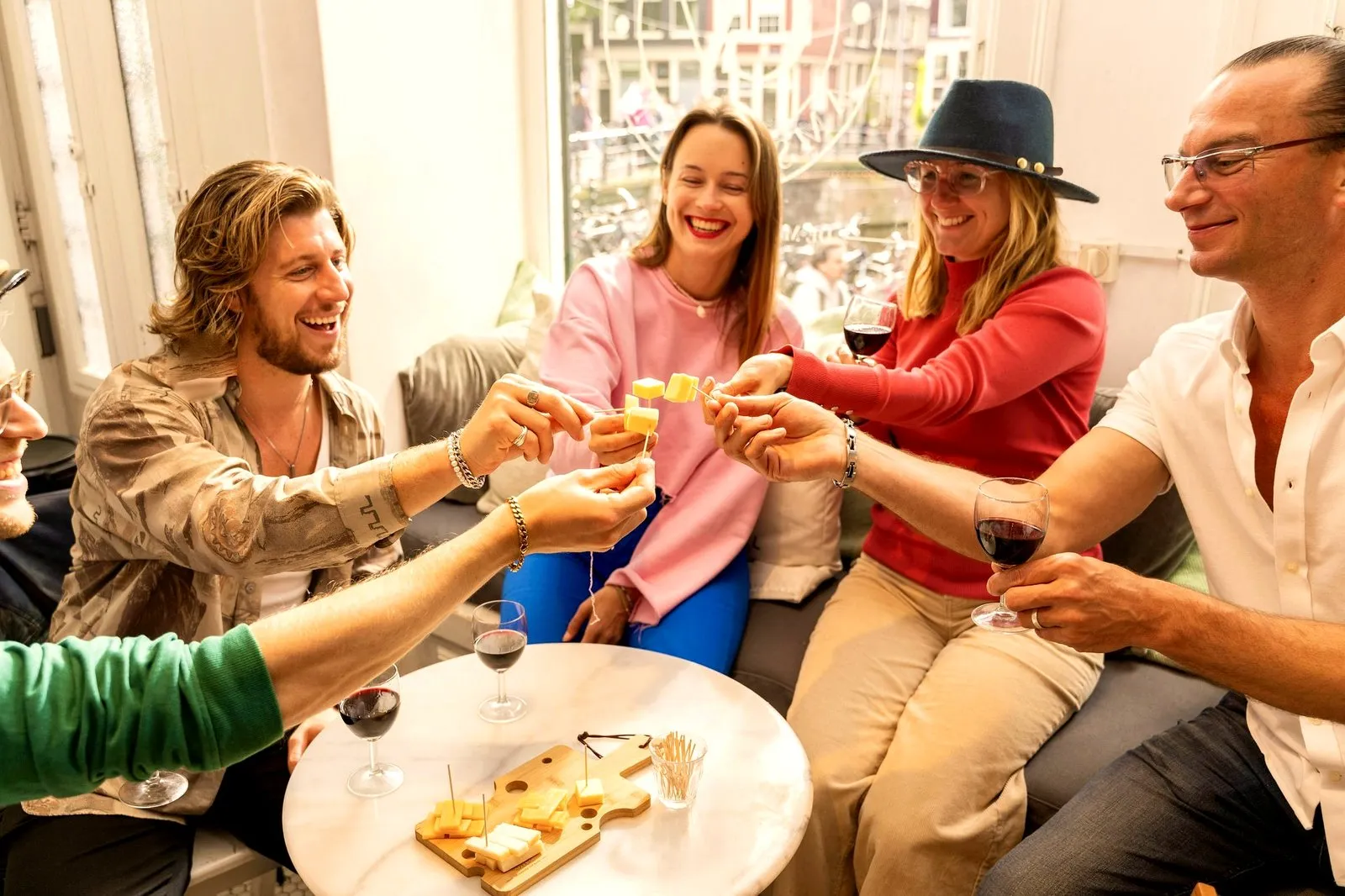 A group of food tour guests toasting red wine and cheese around a table in a sunny Amsterdam canal-house lounge
