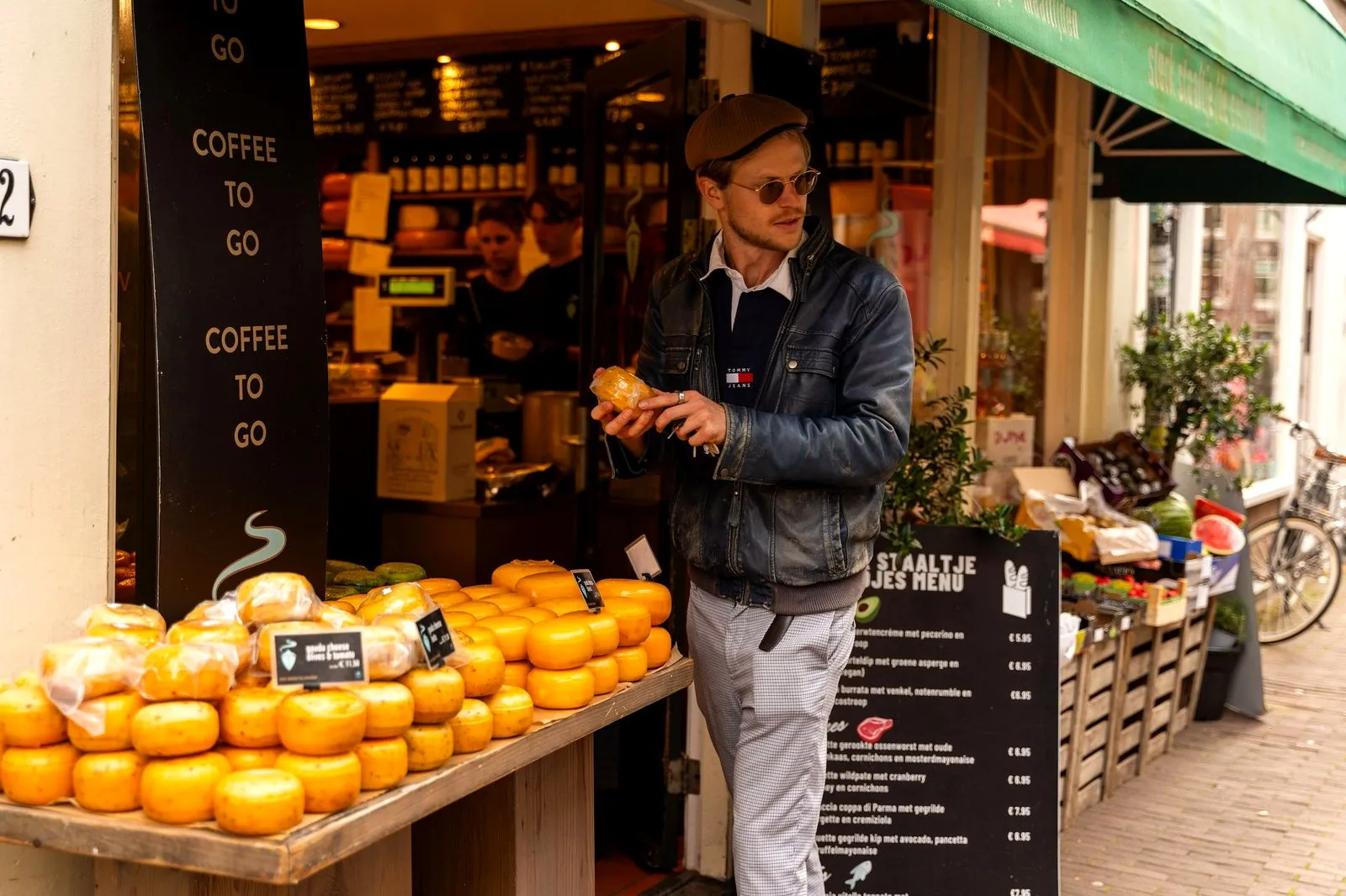 A guest holding a cheese by a display of Gouda wheels outside an Amsterdam cheese shop