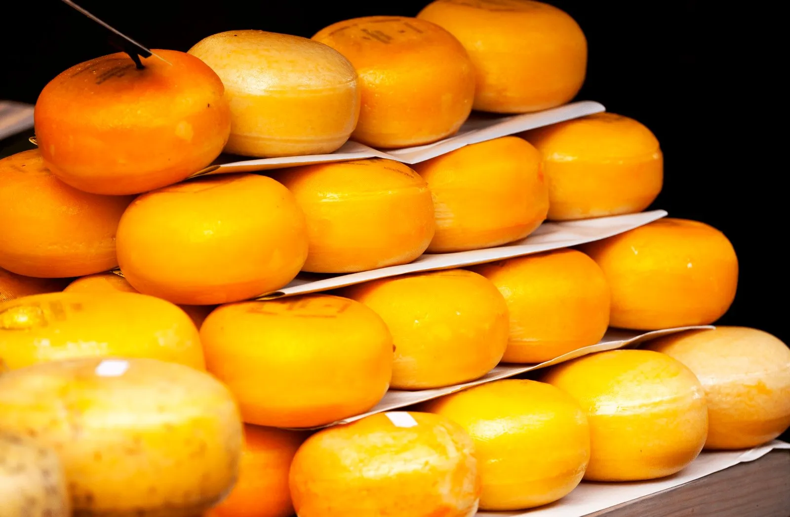 Stacked orange-rind Dutch cheese wheels on a market display