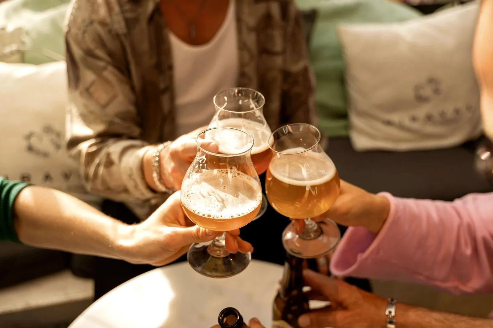 Three hands toasting tulip glasses of craft beer over a table in Amsterdam