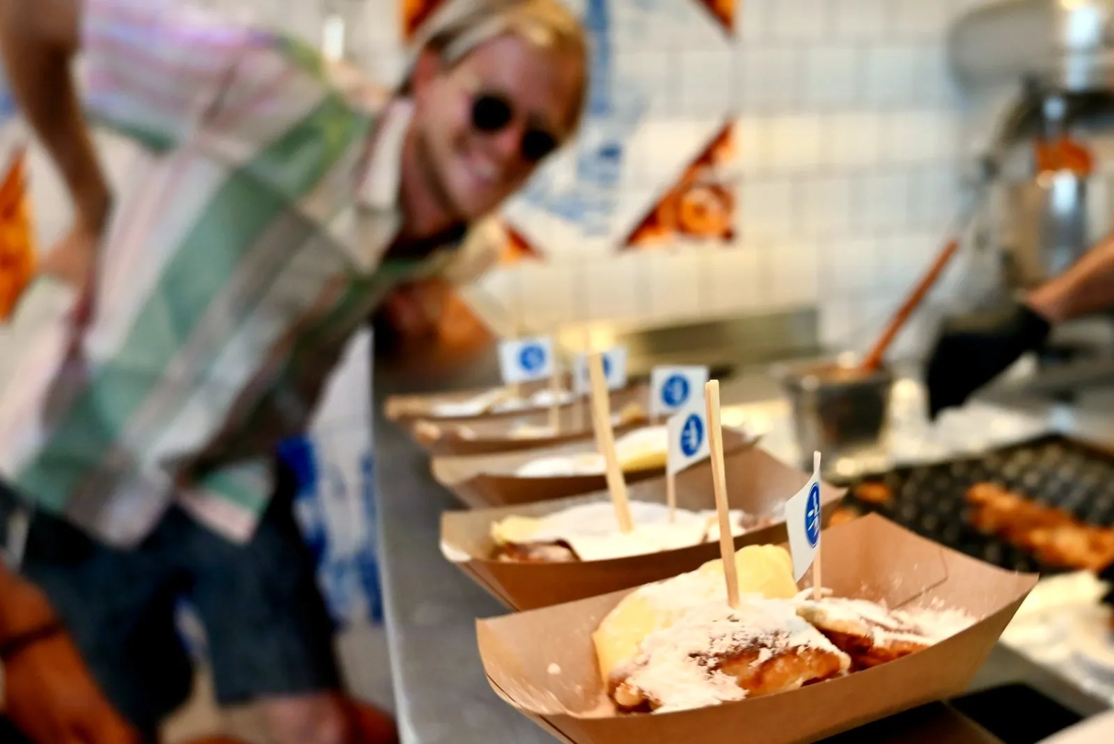 Vendor serving food in paper trays with little flags at a counter