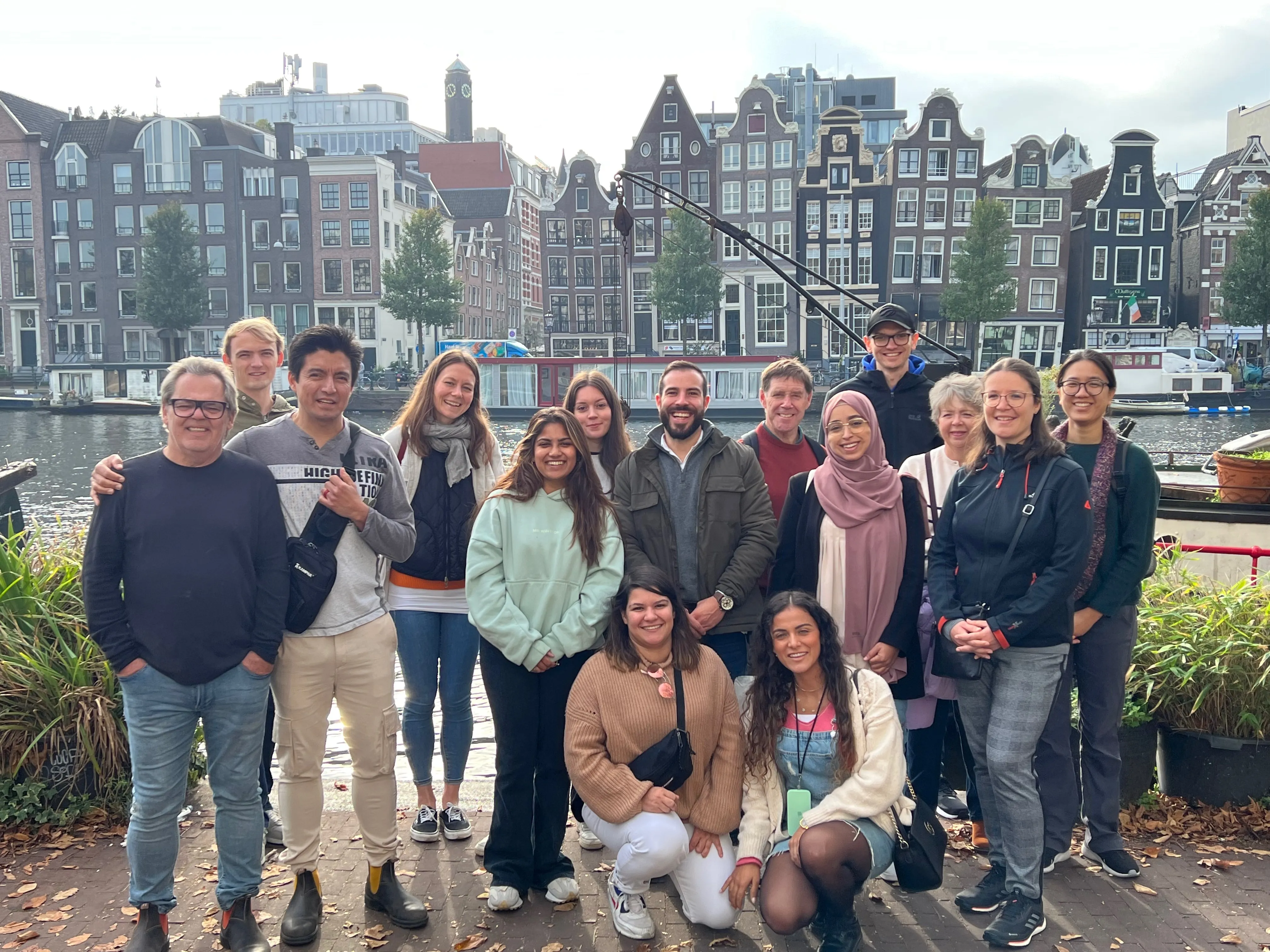 A large food tour group posing by the Amstel river with crooked canal houses behind them