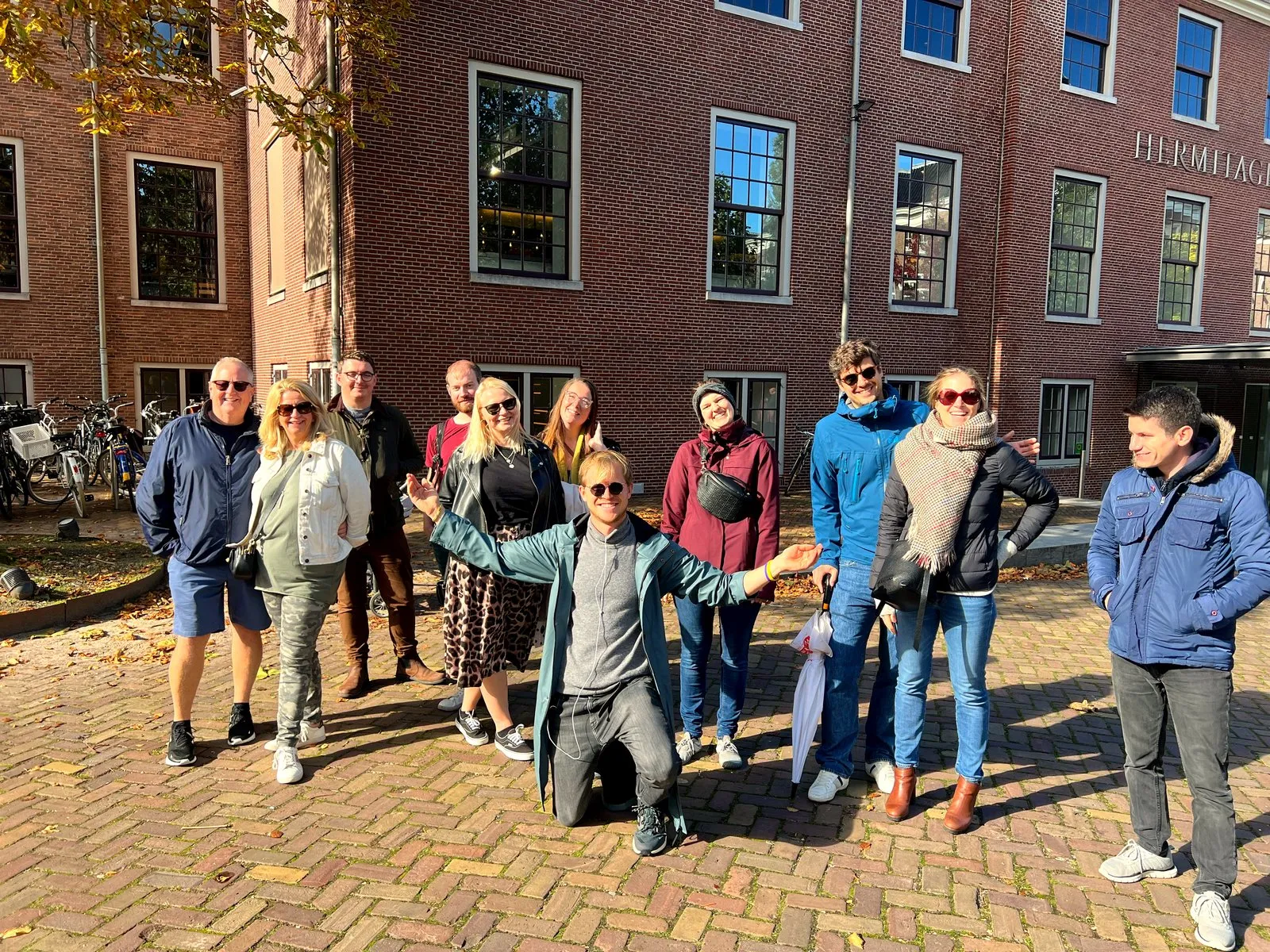A mixed-age food tour group posing with their guide in front of the Hermitage Amsterdam museum
