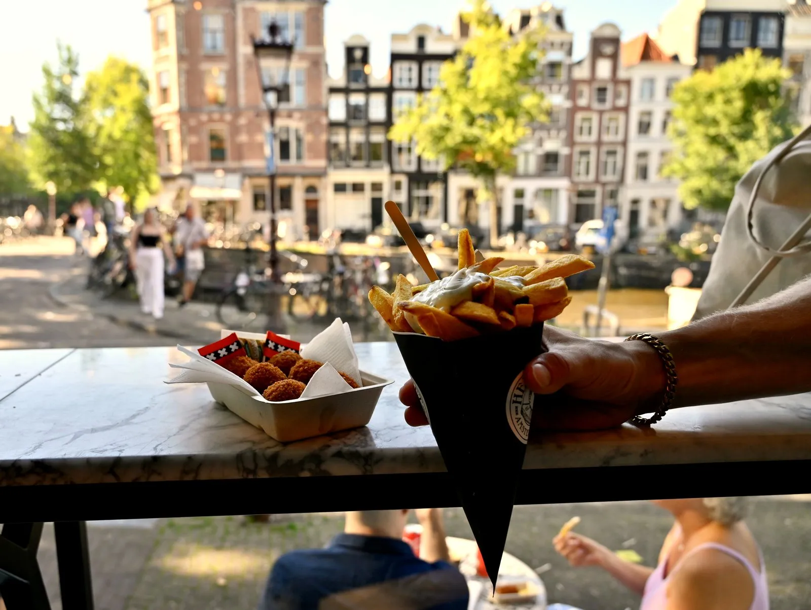 Hand holding fries with mayo and a tray of bitterballen with Amsterdam canal houses behind