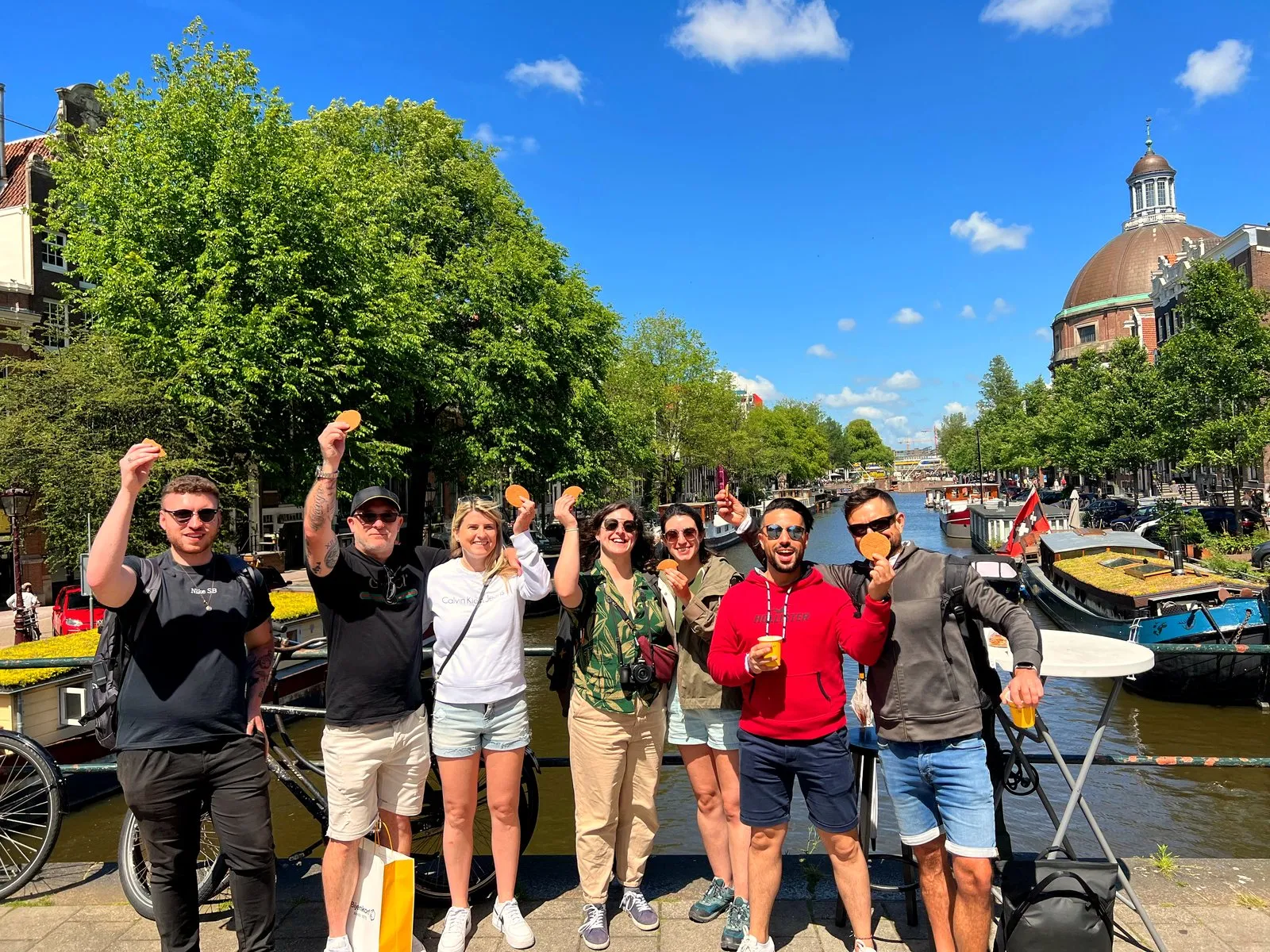 Seven guests holding up stroopwafels together on an Amsterdam canal bridge