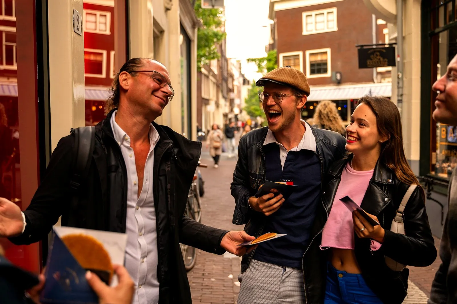 Food tour guide handing a tasting to smiling guests on a busy Amsterdam street
