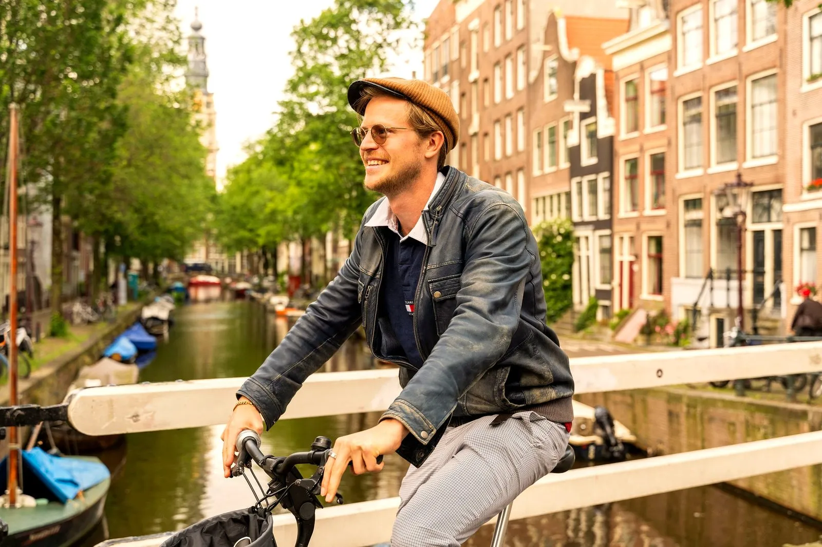 A smiling guide riding a bike over an Amsterdam canal bridge in summer