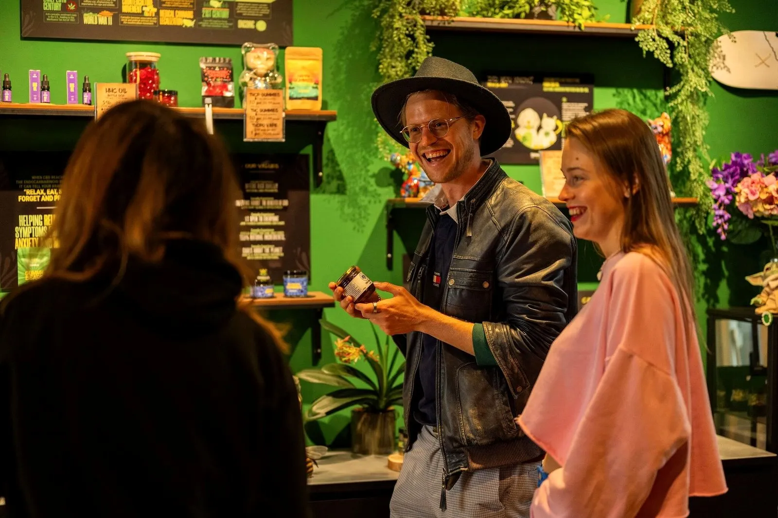 A guide laughing while showing a jar to guests in a green Amsterdam herbal shop