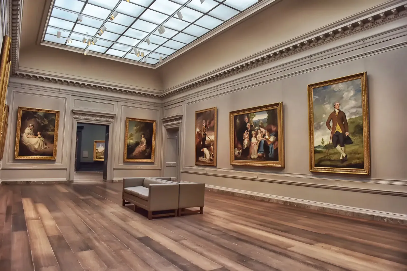 Quiet museum gallery with classical portraits in gilded frames, a skylight ceiling, and a bench in the middle