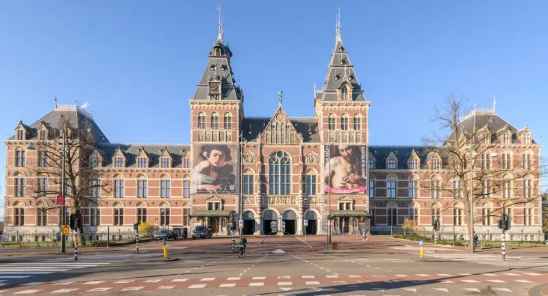 Front facade of the Rijksmuseum in Amsterdam with its twin towers and exhibition banners under a clear blue sky