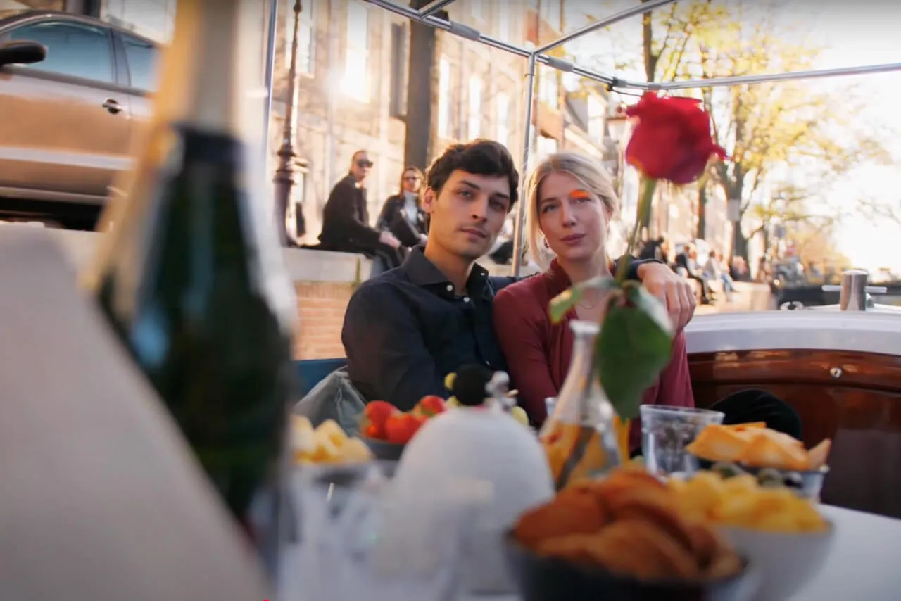A couple with a red rose and a spread of food and bubbles on a private canal boat at golden hour