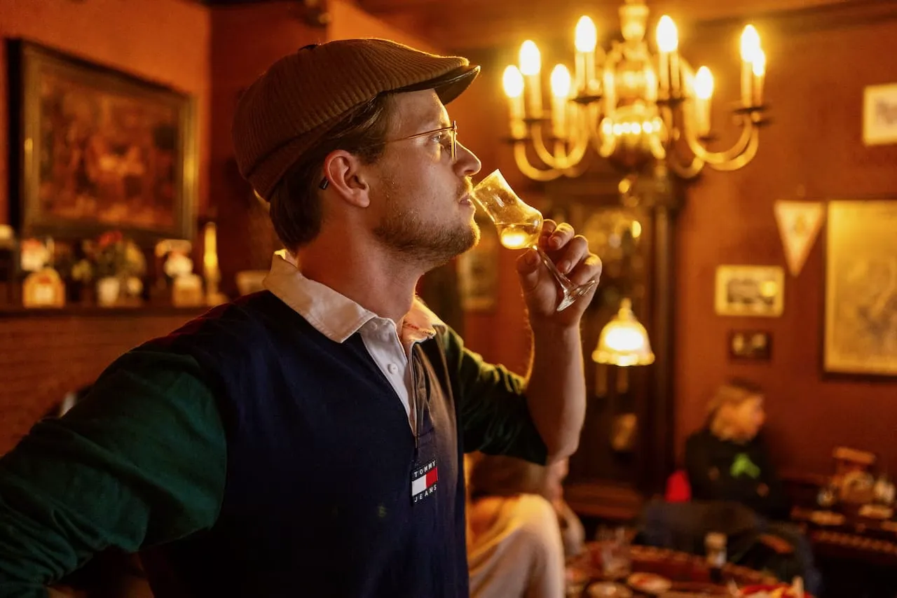 A guest tasting a glass of jenever under a candle chandelier in a historic Amsterdam tasting bar