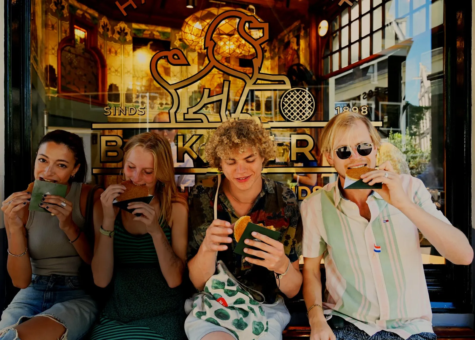 Four food tour guests eating fresh stroopwafels outside a historic Amsterdam bakery