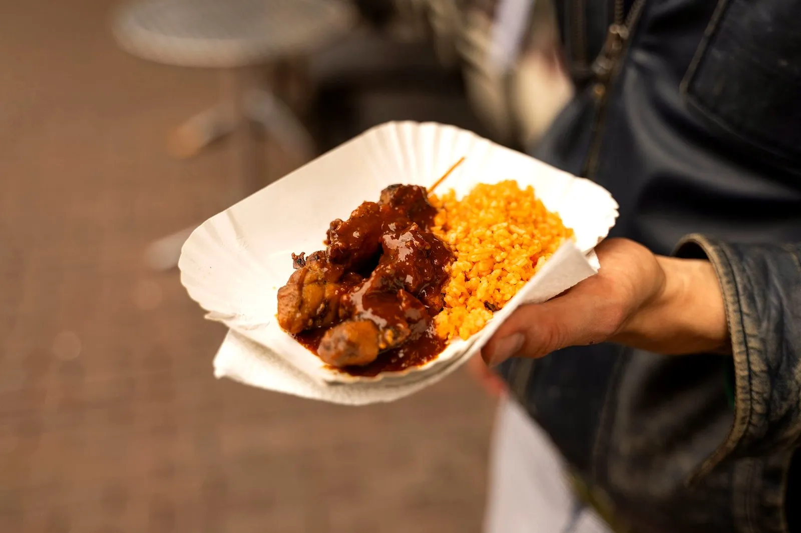 A hand holding a tray of Surinamese chicken with sauce and yellow rice on an Amsterdam street