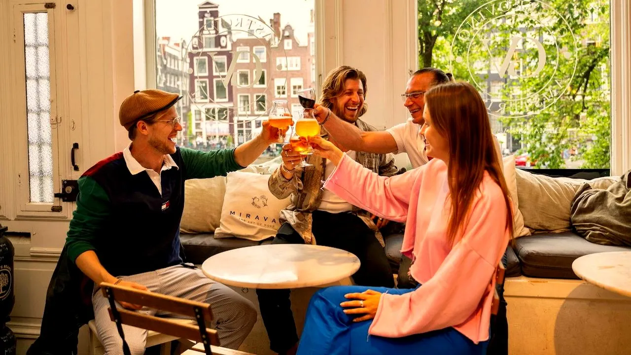 A team of four colleagues toasting craft beer by a canal-view cafe window in Amsterdam