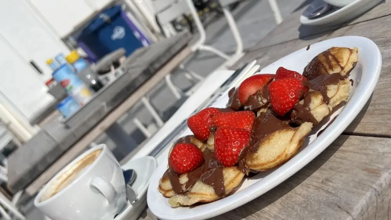 Dutch mini pancakes topped with chocolate and fresh strawberries served with coffee at an outdoor café.