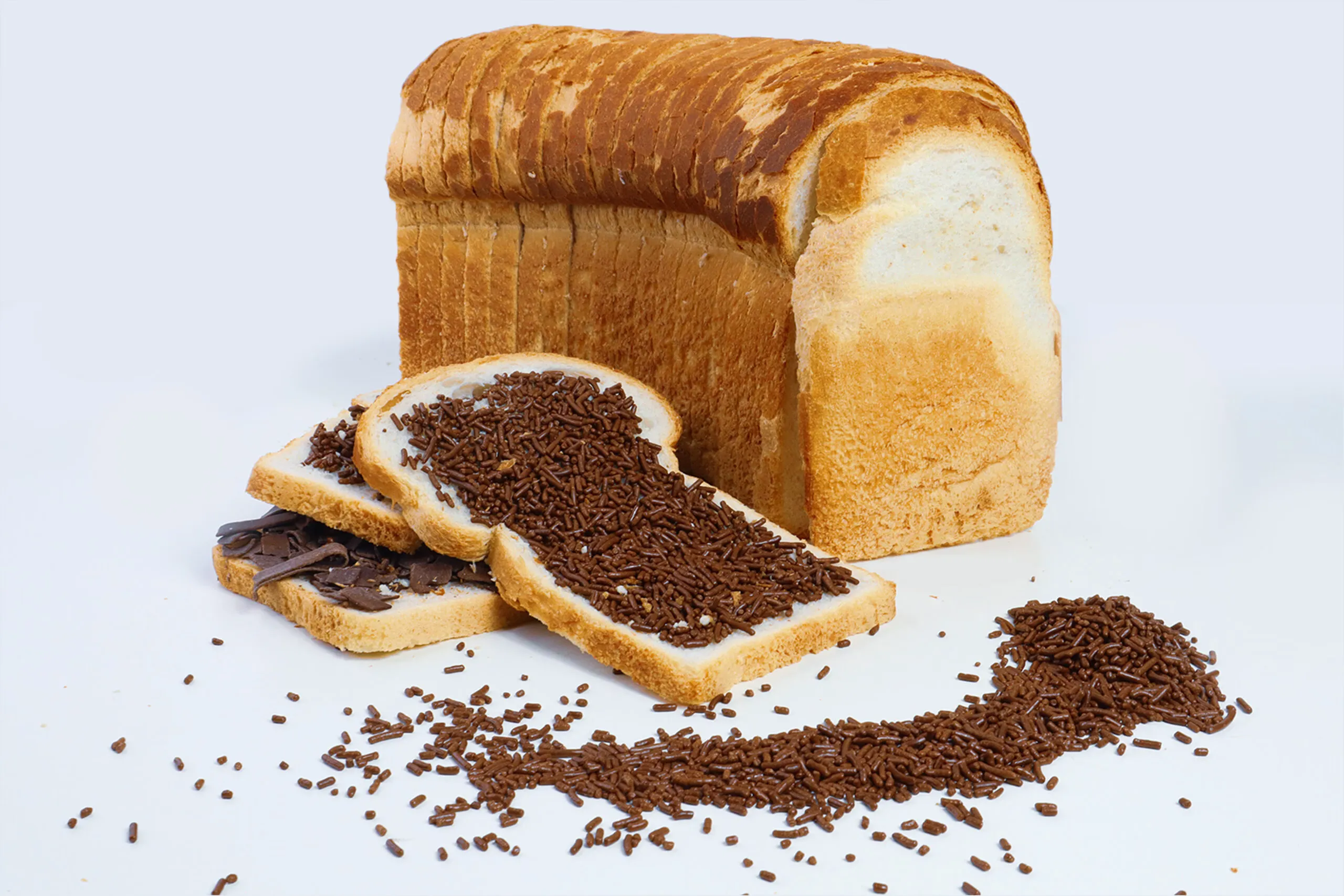Sliced white bread loaf with slices covered in chocolate sprinkles and chocolate spread, loose hagelslag scattered around