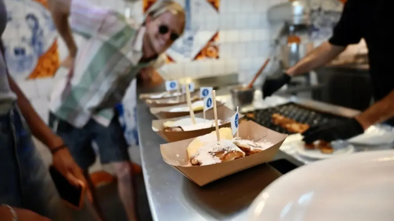 People enjoying fresh stroopwafels at a local Amsterdam food stall while watching them being prepared in a traditional kitchen