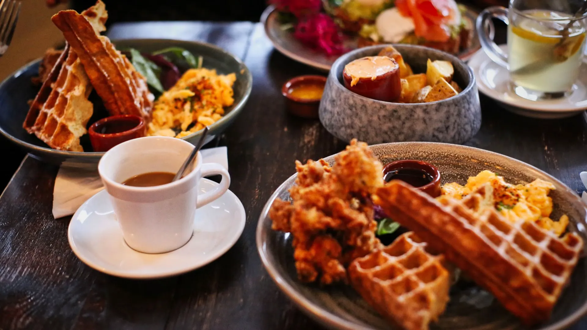 Brunch table with waffles, fried chicken, scrambled eggs and a cup of coffee on a dark wooden table