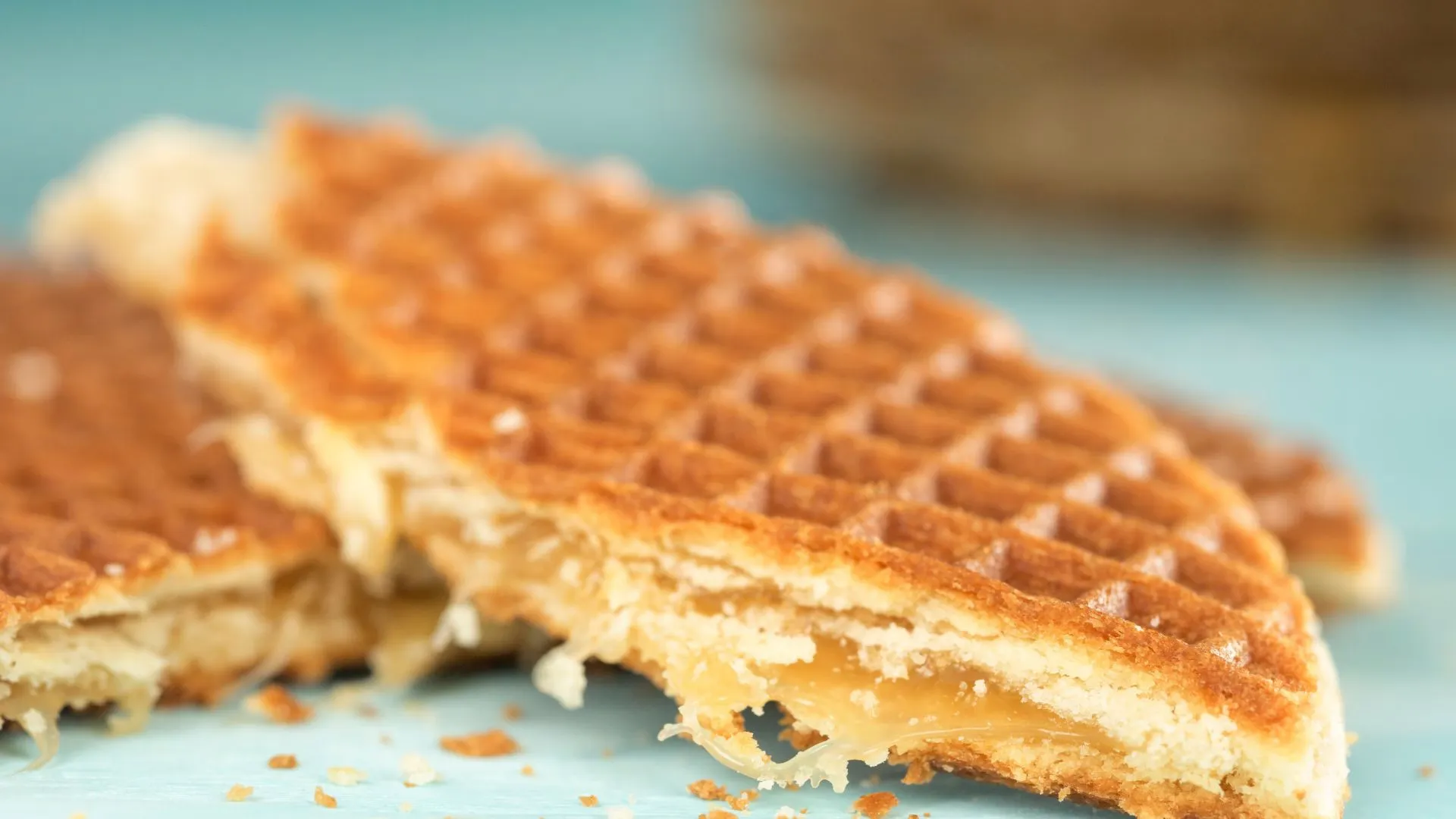 Close-up of a stroopwafel broken in half showing the sticky caramel syrup layer inside, on a light blue surface
