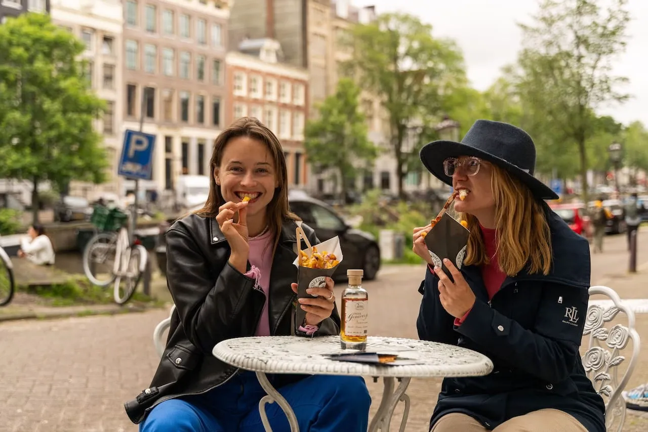 Two guests eating Dutch fries at a canal-side table on an Amsterdam food tour