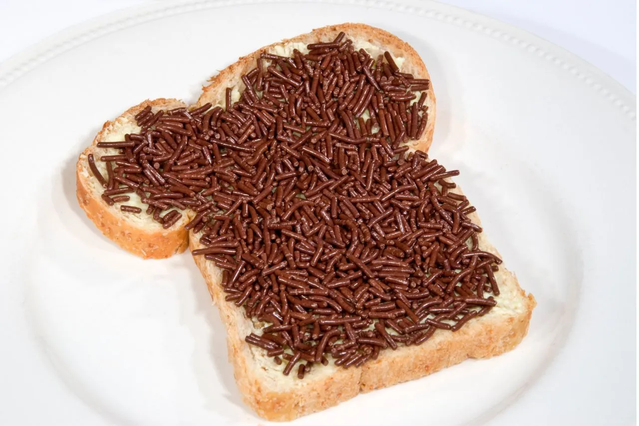 Slice of buttered white bread thickly covered in chocolate sprinkles on a white plate