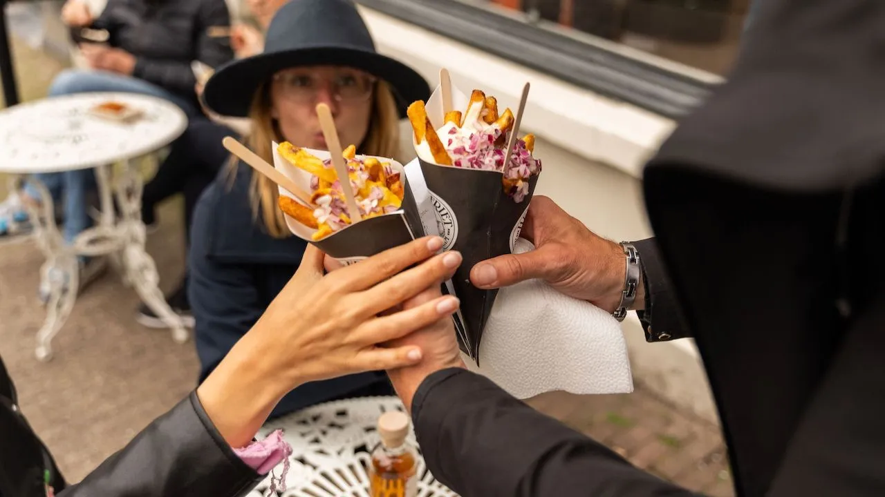 Hands raising paper cones of loaded fries together in a toast at an outdoor cafe table