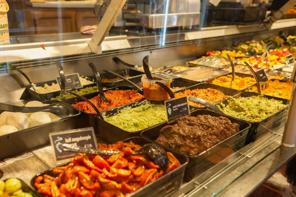 Deli display case filled with trays of fresh salads, spreads and marinated vegetables, each with a small price sign