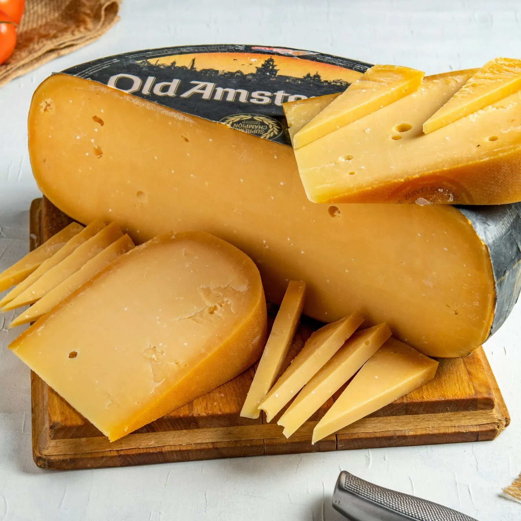 Wheel of Old Amsterdam aged cheese with black rind, cut into wedges and thin slices on a wooden board
