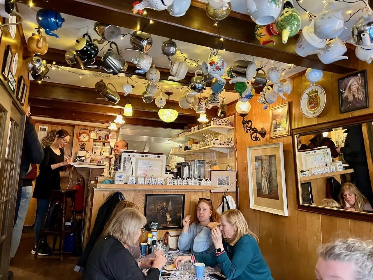 Cozy Amsterdam pancake house interior with dozens of teapots hanging from the ceiling and guests eating at small tables