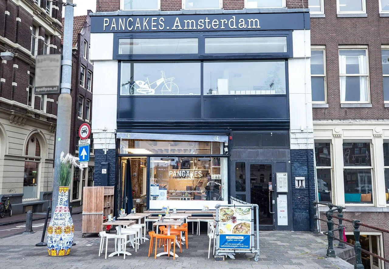 Exterior of the PANCAKES Amsterdam restaurant with a dark facade, outdoor tables and orange chairs