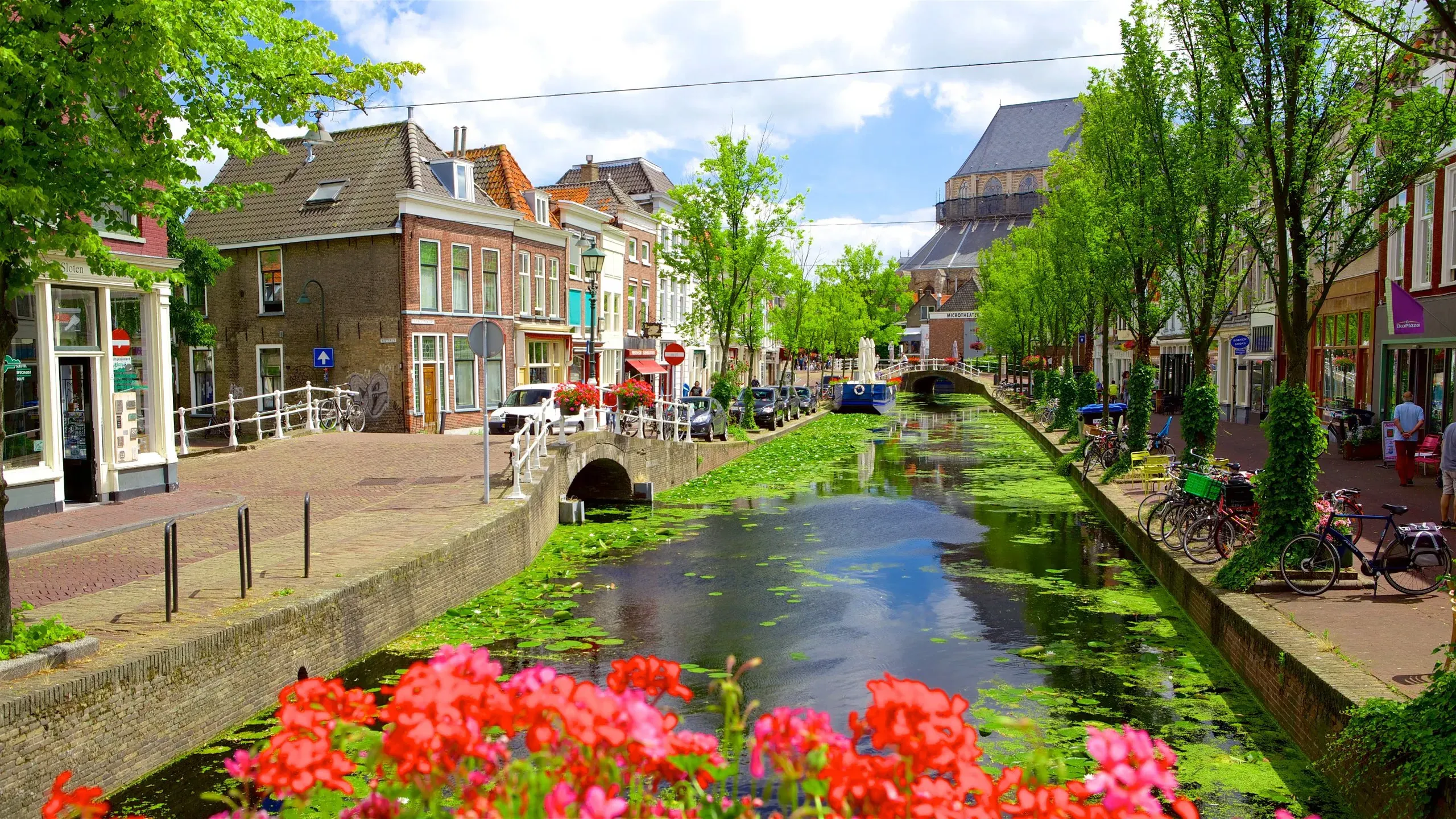 Canal in a Dutch town lined with brick houses, parked bicycles and bright red flowers in the foreground