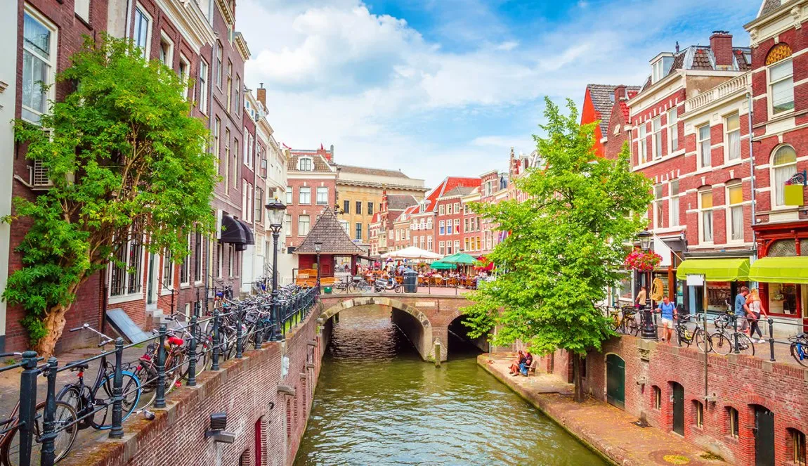 The Oudegracht canal in Utrecht with brick wharf walls, parked bicycles, leafy trees and terraces along the water