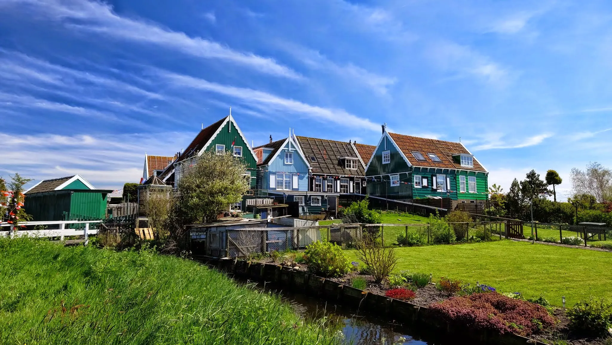 Traditional green and blue wooden houses with tiled roofs in a Dutch Waterland village under a bright blue sky
