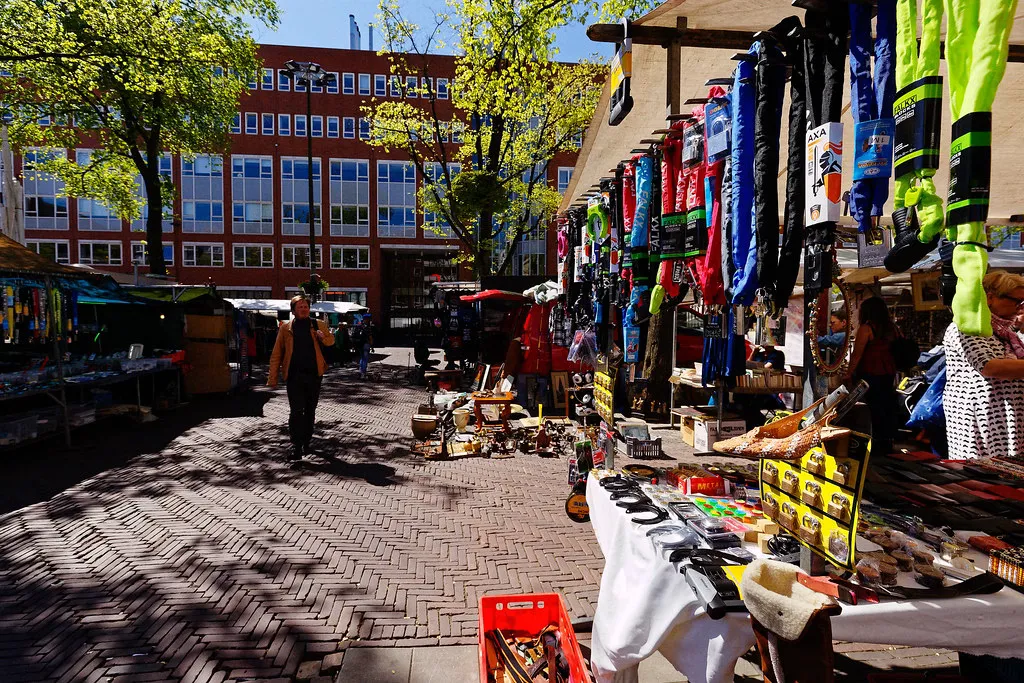 Sunny market square at Waterlooplein in Amsterdam with stalls selling clothing and bric-a-brac on herringbone brick paving
