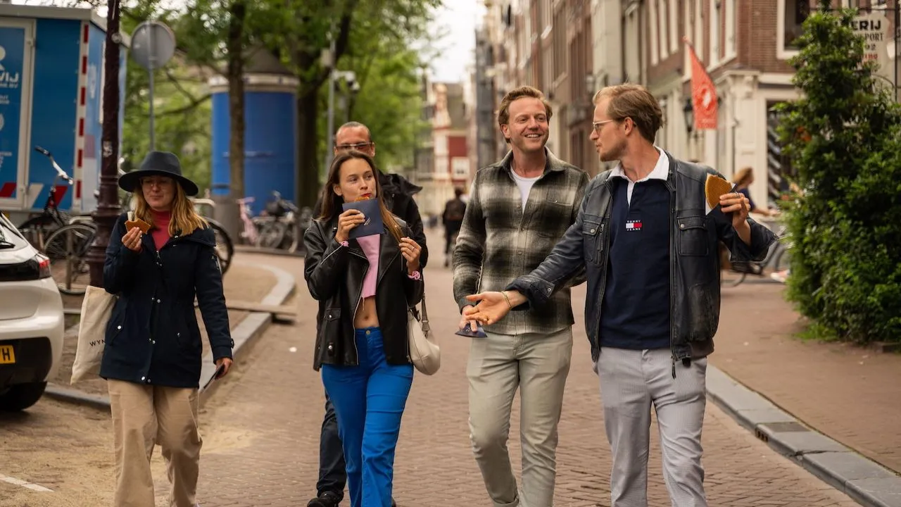 Small group walks down an Amsterdam street eating snacks and chatting with their guide
