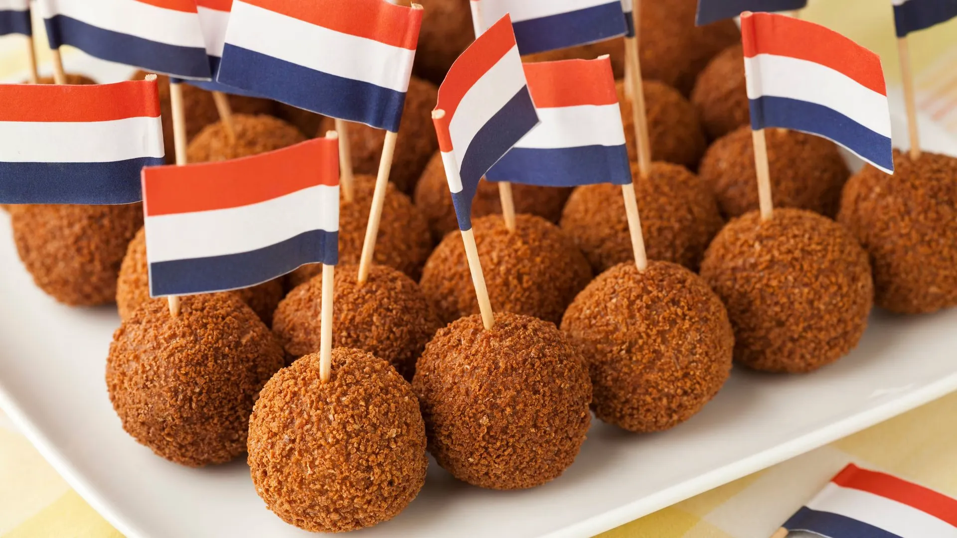 Platter of round fried bitterballen, each skewered with a small Dutch flag on a cocktail stick